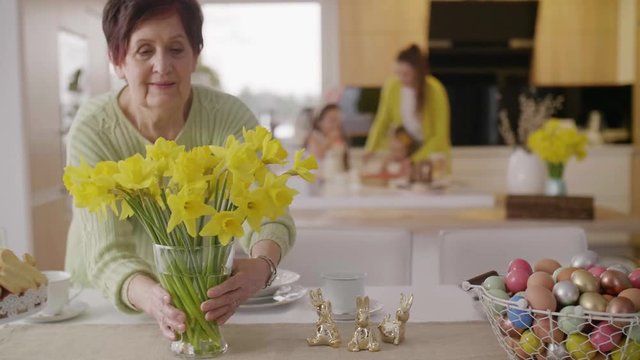 Cheerful grandmother arranging flower at kitchen 