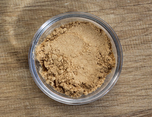 Glass bowl with ginger powder on wooden background