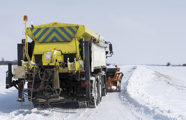 snow-clearing truck on the road sprinkles aggregate and salt