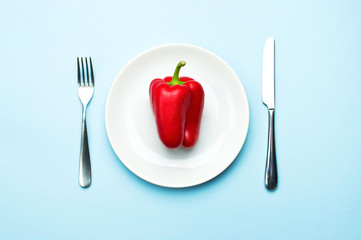 Red bell pepper on a white plate, fork and knife, dieting, healthy food concept. Fresh pepper, health. Food creative concept. Top view Blue Background Flat Lay with copy space