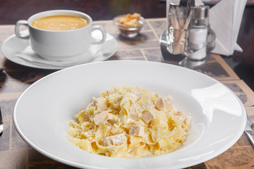 Pasta, noodles with chicken, turkey, decorated with cheese. Serving a meal in a cafe, restaurant. Side view. In the background, soup and crackers, croutons and cutlery