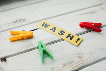 Wash inscription and colorful clothes pegs on a white wooden background
