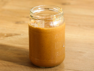 Glass jar pot with homemade peanut butter on wooden background