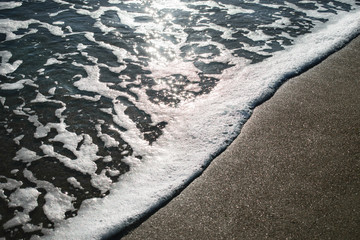 a foamy wave comes to the shore with golden sand. evening sea surf. glare of the sun on the water....