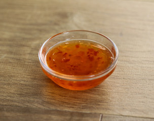 Bowl with sweet and sour chili sauce on wooden background