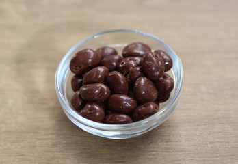 Glass bowl with Belgian chocolate raisins on wooden background