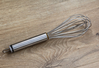 Metal balloon whisk in kitchen on wooden background