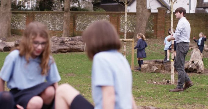 4k, Group of young boys and girls playing in a school yard during lunch break under the watchful eyes of the head teacher. Slow motion.