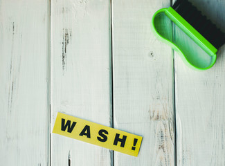 Cleaning house or office concept. Green cleaning brush and WASH inscription on a white wooden...