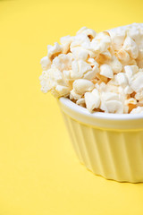 Bright yellow background. Fresh pop corn. Small white bowl