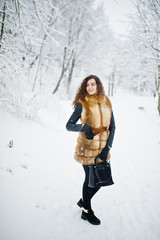 Fototapeta na wymiar Elegance curly girl in fur coat and handbag at snowy forest park at winter.