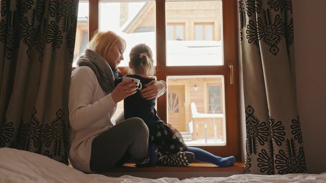 woman sits on the windowsill and hugs her daughter