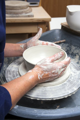 A lady ceramics artist at work in her home pottery studio, throwing a bowl on a wheel