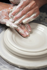 A lady ceramics artist at work in her home pottery studio, throwing a bowl on a wheel. Opening up.