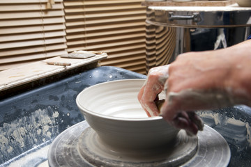 A lady ceramics artist at work in her home pottery studio, throwing a bowl on a wheel.