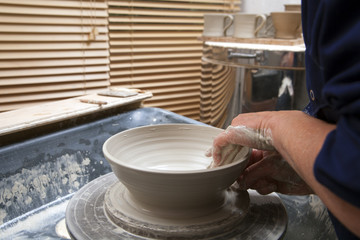 Fototapeta na wymiar A lady ceramics artist at work in her home pottery studio, throwing a bowl on a wheel