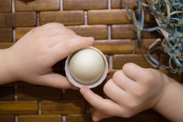 Fototapeta na wymiar child's hands holding eggs in a paper nest and a cup as a symbol of easter