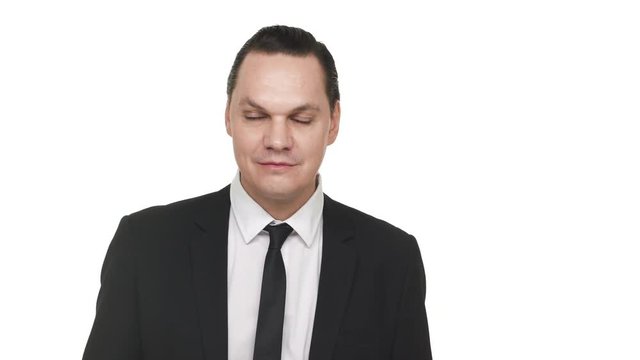 Portrait of adult man in classic black suit smirking and behaving sarcastically, over white background in studio. Concept of emotions