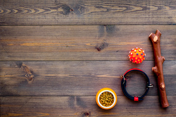 Pet accessories. Toys near bowls with animal feed, collar on dark wooden background top view copy space