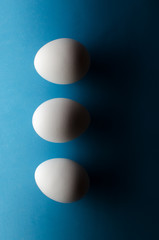 Three white chicken eggs on black and blue background. The concept is black and white stripe.
