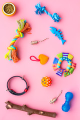 Pet accessories. Toys near bowls with animal feed, grooming equipment on pink background top view