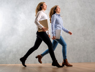 Business Frauen mit Buch und Laptop springen  eilig vor Betonwand
