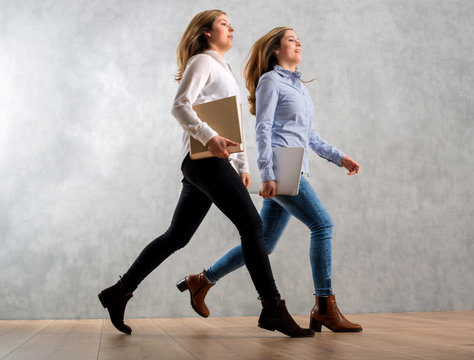 Business Frauen mit Buch und Laptop springen  eilig vor Betonwand