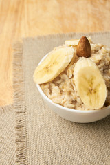Oatmeal with almonds and banana. White bowl. Neutral background