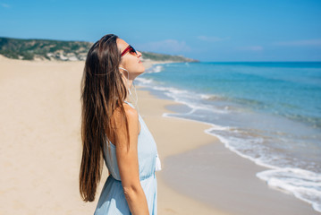 Girl in sunglass is standing on the beach and listening musi