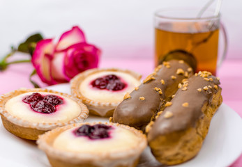 Different cakes with custard and cream and berries on a white plate with tea in the background.