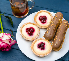 Different cakes with custard and cream and berries on a white plate with tea in the background.