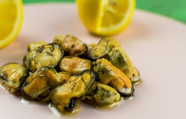 Mussels on a pink-lilac-colored plate on a wooden green background.