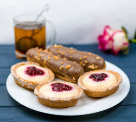 Different cakes with custard and cream and berries on a white plate with tea in the background.