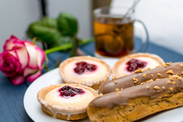 Different cakes with custard and cream and berries on a white plate with tea in the background.