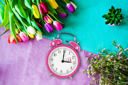 Switch to summer time on alarm clock with tulips and flowers from above