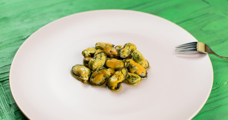 Mussels on a pink-lilac-colored plate on a wooden green background.