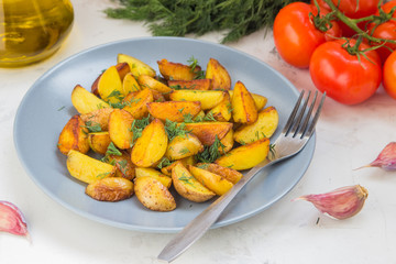Fried potatoes in a plate. Baby potatoes, green, tomatoes and garlic on the table