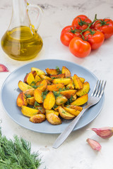 Fried potatoes in a plate. Baby potatoes, green, tomatoes and garlic on the table