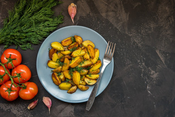 Fried baby potatoes, green, tomatoes and garlic on a dark background