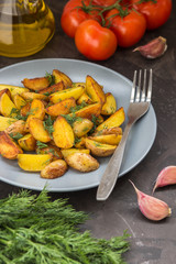 Fried baby potatoes, green, tomatoes and garlic on a dark background