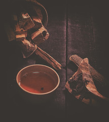 The classic old film design background of clay tea cup put at the middle of wooden herb sticks and dried tea leaves,on wooden timber board,abstract art design,blurry around.