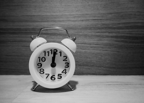 The white alarm clock put on wooden timber board,in vintage and art design,black and white tone,grainy film style,