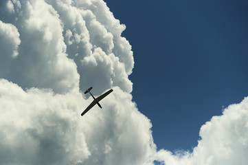 A Glider flying in blue sky with big white clouds. The glider is a plane that has no engine
