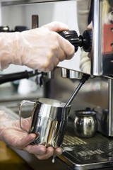 A barista at a cafe churns milk in a metal jug using a caper of  professional coffee machine. Coffee house concept. The process of making cappuccino or latte