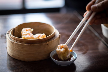 hand with chopstick holding dimsum in to soy sauce
