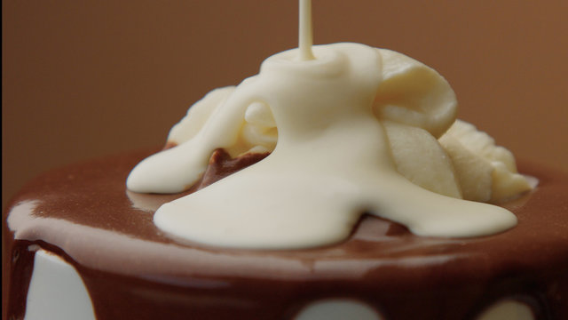cup of hot chocolate with a cream and liquid white chocolate pouring on it. CLoseup