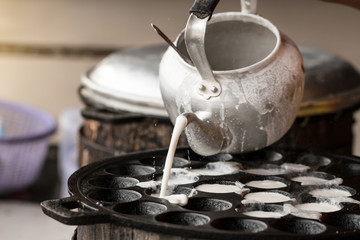Pouring coconut milk into a stove preparing for Thai sweetmeat or Coconut-rice pancakes (Kanom Krok) - obrazy, fototapety, plakaty