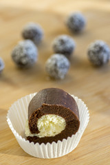 chocolate coconut balls and roulade decorated with shredded coconut on wooden bamboo table