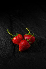 Fresh red strawberry on black stone plate in dark background