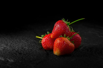 Fresh red strawberry on black stone plate in dark background